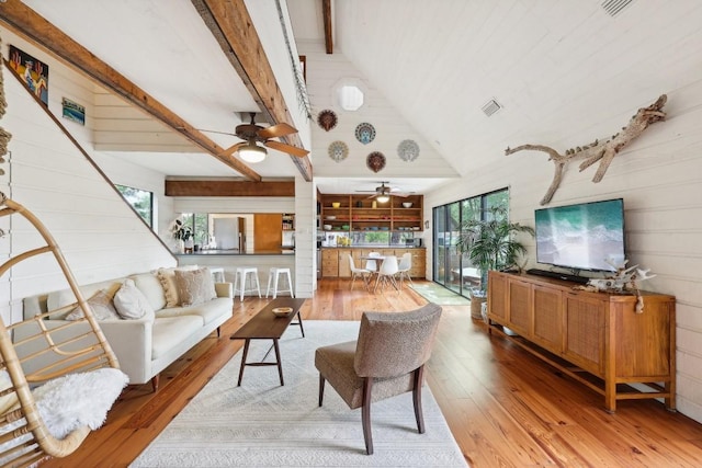 living room featuring light hardwood / wood-style flooring, a wealth of natural light, wooden walls, and beamed ceiling