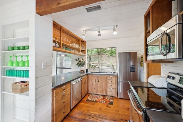 kitchen with appliances with stainless steel finishes, wood walls, rail lighting, sink, and light hardwood / wood-style flooring