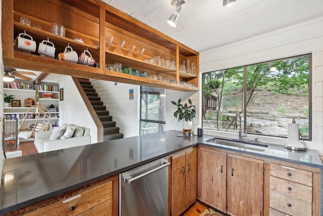 kitchen with sink, stainless steel dishwasher, ceiling fan, and wood walls