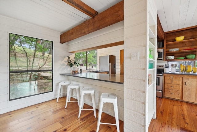 kitchen featuring stainless steel appliances, wood walls, beam ceiling, and light hardwood / wood-style flooring