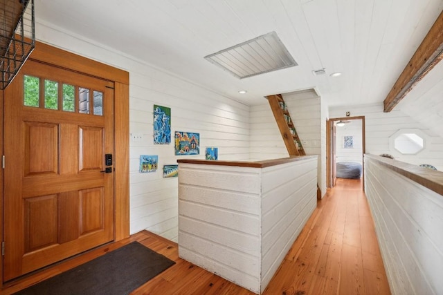 entryway featuring beam ceiling, wooden walls, and light wood-type flooring