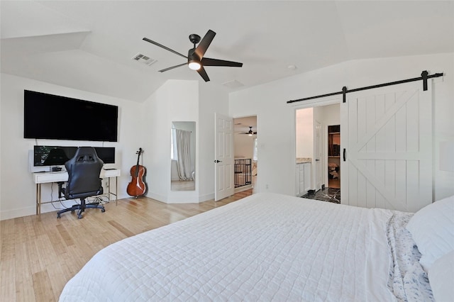 bedroom featuring ceiling fan, ensuite bathroom, vaulted ceiling, a barn door, and light wood-type flooring