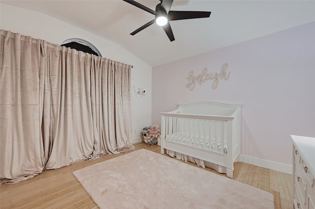 bedroom with a crib, vaulted ceiling, ceiling fan, and light wood-type flooring