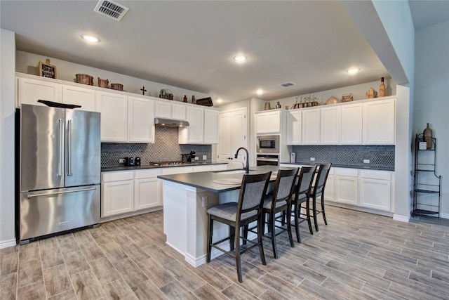 321 Dancing Oak Ln Unit 101, San Marcos, TX 78666 - kitchen featuring stainless steel appliances, under cabinet range hood, dark countertops, decorative backsplash, and a kitchen bar