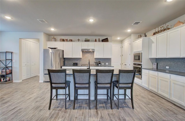 321 Dancing Oak Ln Unit 101, San Marcos, TX 78666 - kitchen featuring appliances with stainless steel finishes, backsplash, white cabinets, a kitchen island with sink, and a kitchen breakfast bar