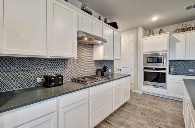 321 Dancing Oak Ln Unit 101, San Marcos, TX 78666 - kitchen with stainless steel appliances, under cabinet range hood, dark countertops, and white cabinets