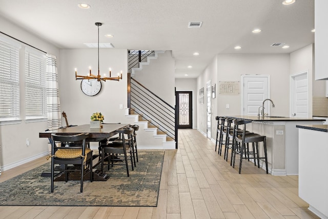 dining room with an inviting chandelier, light hardwood / wood-style floors, sink, and a textured ceiling