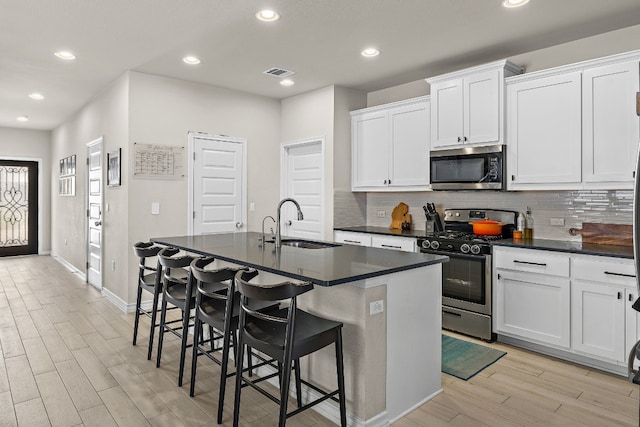 kitchen featuring light wood-type flooring, stainless steel appliances, white cabinets, and a center island with sink