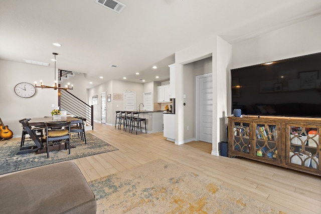 living room featuring an inviting chandelier, sink, and light wood-type flooring