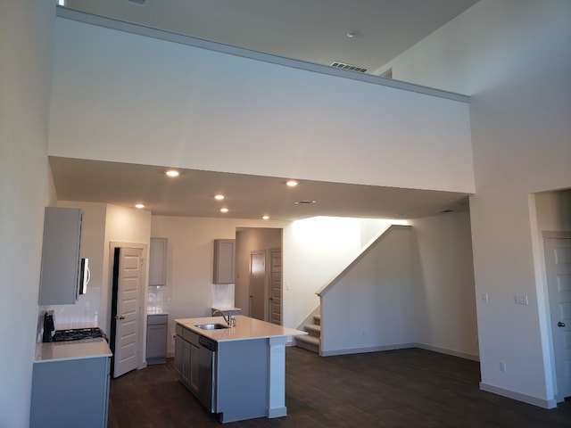 kitchen with sink, a center island with sink, dark hardwood / wood-style floors, stainless steel appliances, and decorative backsplash