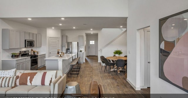 kitchen with hardwood / wood-style flooring, gray cabinetry, a center island with sink, stainless steel appliances, and a kitchen bar