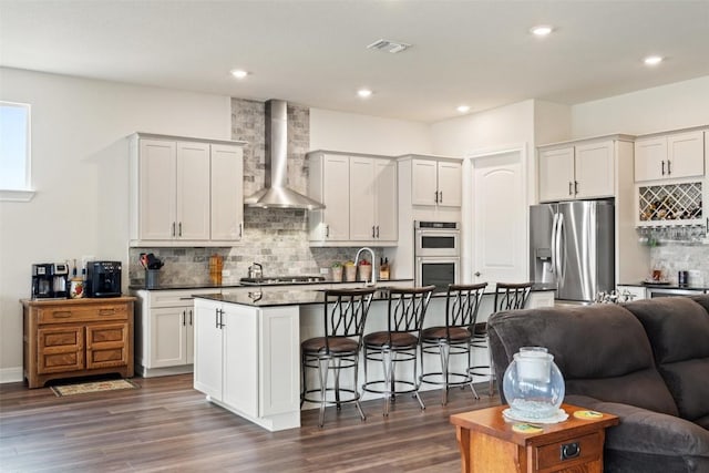 kitchen featuring white cabinetry, stainless steel appliances, wall chimney exhaust hood, and a center island with sink