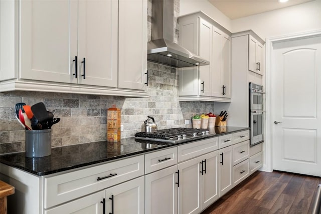 kitchen with white cabinetry, dark stone counters, wall chimney exhaust hood, and appliances with stainless steel finishes