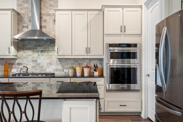 kitchen with wall chimney exhaust hood, appliances with stainless steel finishes, decorative backsplash, and white cabinets