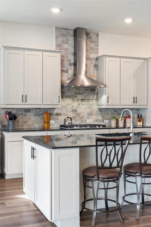 kitchen featuring stainless steel gas cooktop, dark hardwood / wood-style flooring, wall chimney range hood, decorative backsplash, and white cabinets