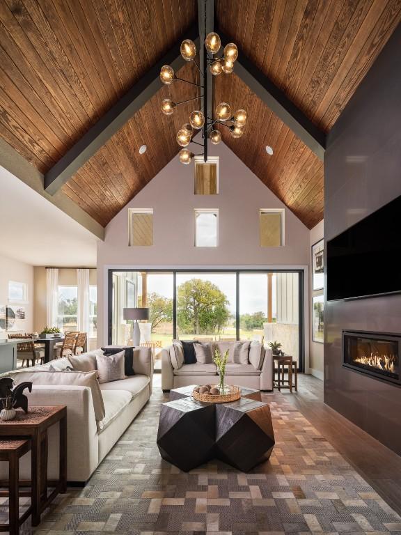 living room featuring a glass covered fireplace, wooden ceiling, an inviting chandelier, carpet, and high vaulted ceiling