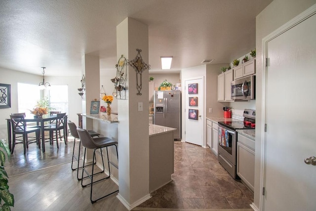 kitchen with appliances with stainless steel finishes, white cabinetry, a kitchen breakfast bar, hanging light fixtures, and light stone countertops