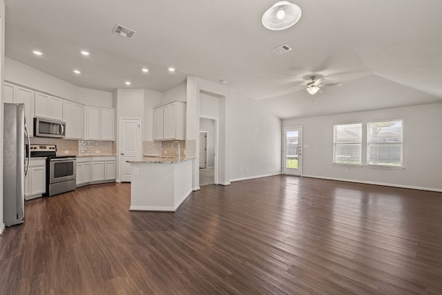 kitchen with dark wood-type flooring, white cabinetry, appliances with stainless steel finishes, light stone countertops, and backsplash