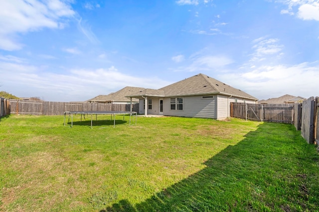 rear view of property with a yard and a trampoline