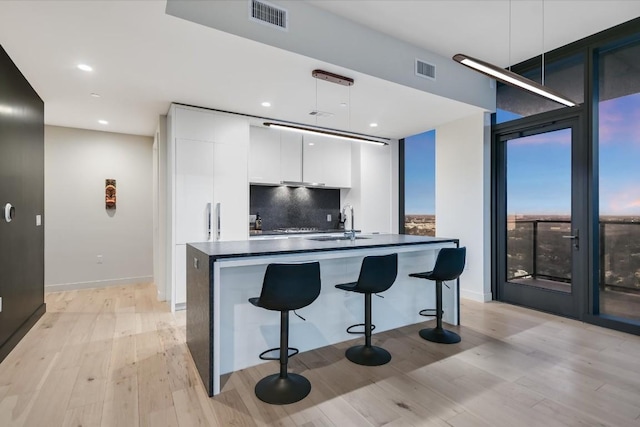 kitchen featuring sink, white cabinetry, hanging light fixtures, backsplash, and light hardwood / wood-style floors