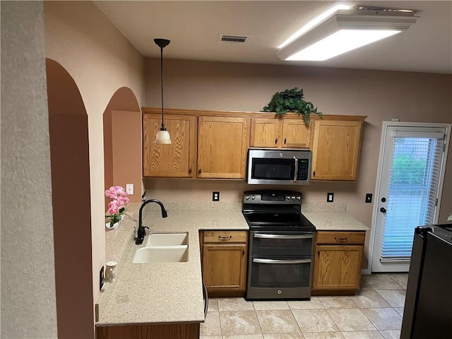 kitchen with light tile patterned flooring, sink, light stone counters, appliances with stainless steel finishes, and pendant lighting