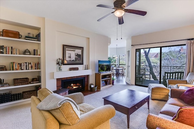 carpeted living room featuring built in features, a tile fireplace, and ceiling fan