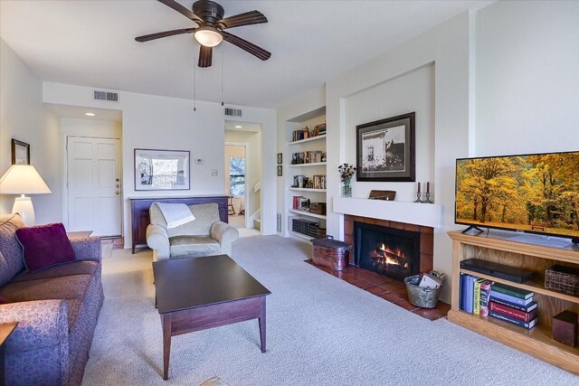 carpeted living room featuring built in shelves, ceiling fan, and a tile fireplace