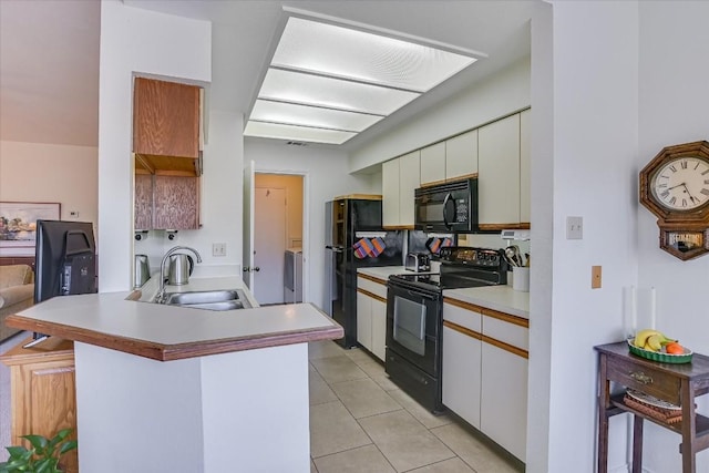 kitchen with light tile patterned floors, a peninsula, light countertops, black appliances, and a sink