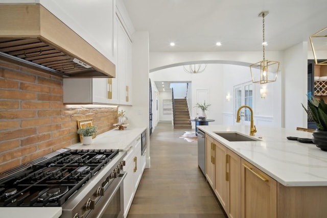 kitchen with sink, custom exhaust hood, hanging light fixtures, light stone countertops, and white cabinets