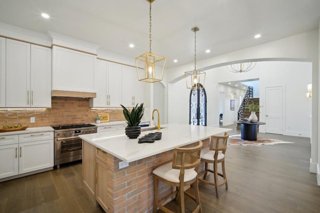 kitchen featuring white cabinetry, high end range, decorative light fixtures, dark hardwood / wood-style flooring, and a kitchen island with sink