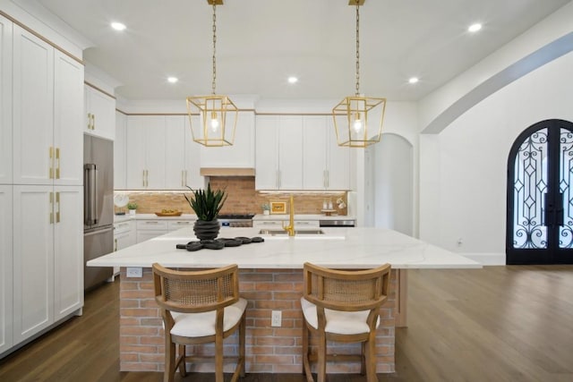 kitchen featuring a breakfast bar, high end fridge, white cabinetry, hanging light fixtures, and an island with sink