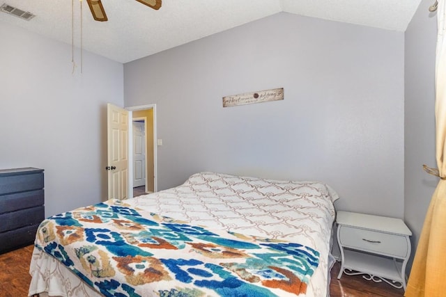 bedroom with ceiling fan, dark hardwood / wood-style floors, vaulted ceiling, and a textured ceiling