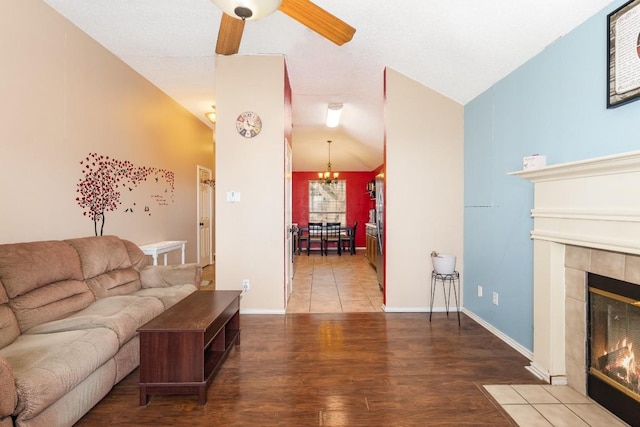 living room featuring a tiled fireplace, vaulted ceiling, wood-type flooring, and ceiling fan with notable chandelier