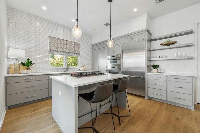 kitchen with gray cabinets, appliances with stainless steel finishes, a breakfast bar area, a center island, and light hardwood / wood-style floors