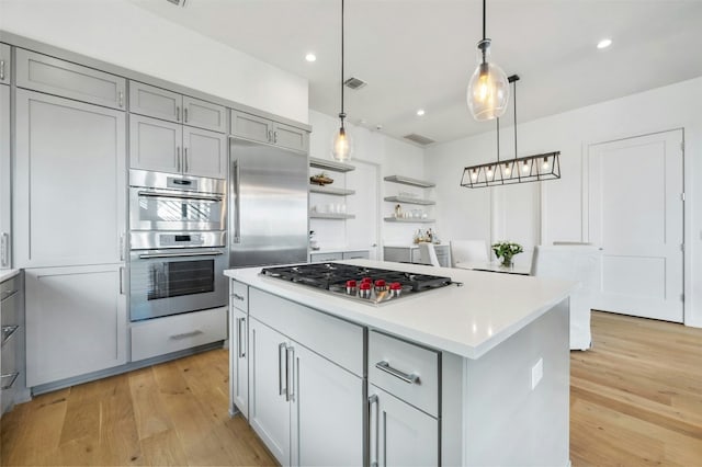 kitchen featuring a kitchen island, appliances with stainless steel finishes, pendant lighting, gray cabinetry, and light hardwood / wood-style flooring