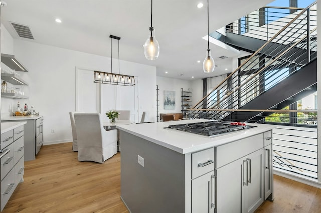 kitchen featuring gray cabinetry, light hardwood / wood-style floors, stainless steel gas cooktop, a kitchen island, and decorative light fixtures