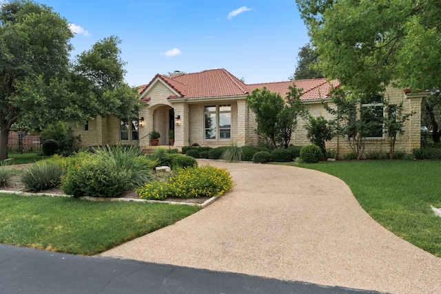 mediterranean / spanish-style home featuring driveway, stone siding, a tile roof, and a front lawn