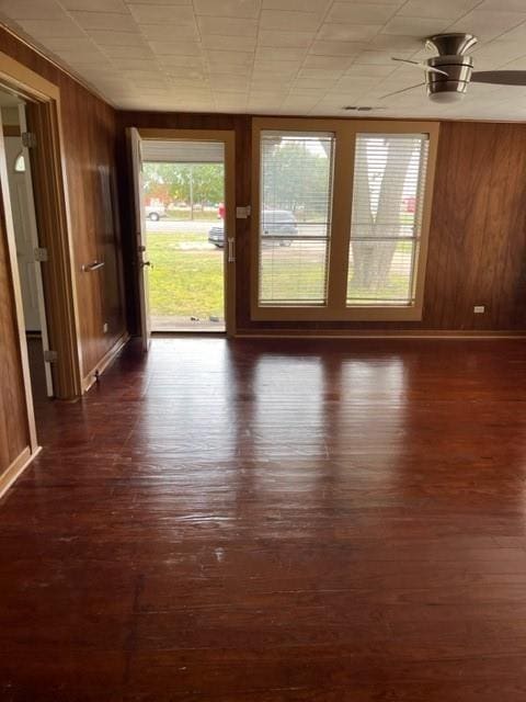 spare room featuring dark wood-type flooring, wooden walls, and ceiling fan