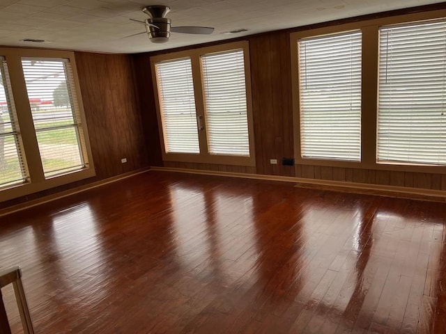 empty room featuring ceiling fan, dark hardwood / wood-style floors, and wood walls