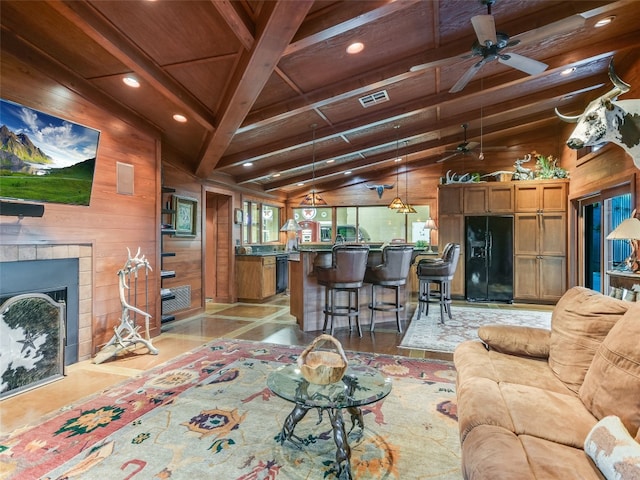 living room with wood walls, wood ceiling, lofted ceiling with beams, ceiling fan, and a tiled fireplace