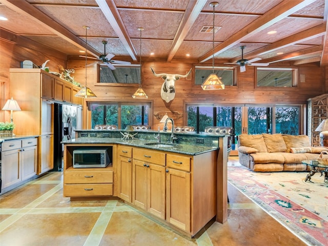 kitchen with pendant lighting, sink, ceiling fan, dark stone countertops, and wooden walls