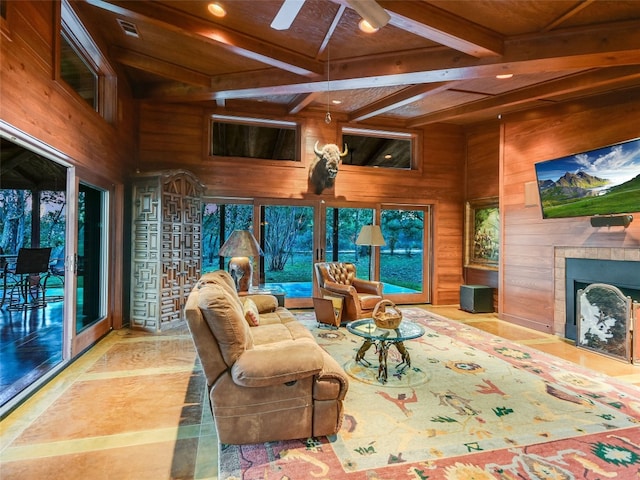 living room with ceiling fan, beam ceiling, a high ceiling, a fireplace, and wood walls