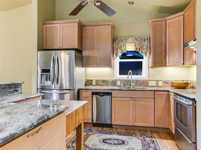 kitchen featuring vaulted ceiling, decorative light fixtures, sink, light stone counters, and stainless steel appliances