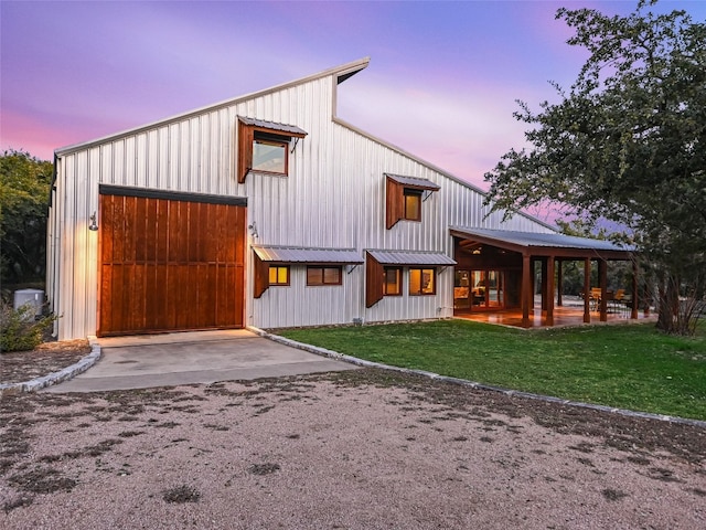 exterior space featuring driveway, a detached garage, metal roof, and a lawn