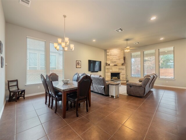 tiled dining area with ceiling fan with notable chandelier and a stone fireplace