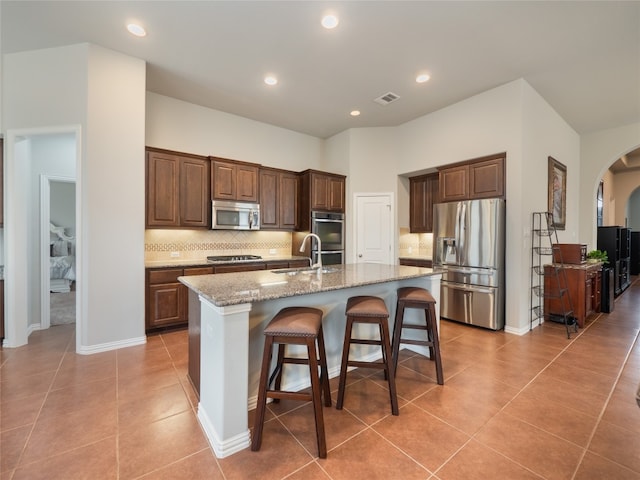 kitchen featuring a center island with sink, tasteful backsplash, a kitchen breakfast bar, stainless steel appliances, and light stone countertops