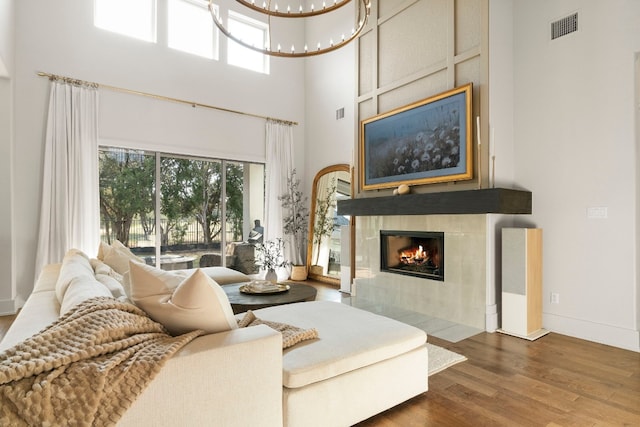 living room featuring a high ceiling, a tile fireplace, dark wood-type flooring, and a chandelier