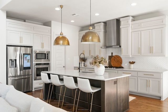 kitchen featuring sink, stainless steel appliances, a center island with sink, decorative light fixtures, and wall chimney exhaust hood