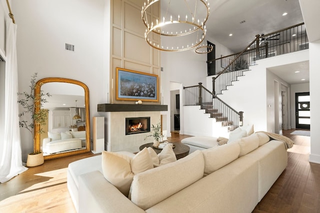 living room featuring a high ceiling, wood-type flooring, an inviting chandelier, and a fireplace