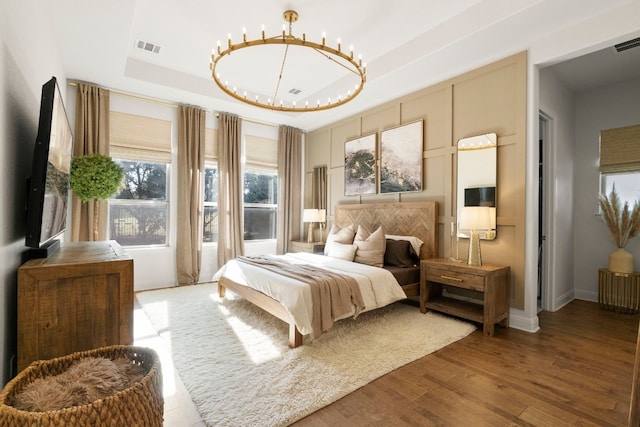 bedroom with wood-type flooring, a chandelier, and a tray ceiling